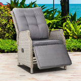 Grey wicker recliner chair with footrest extended on a paved patio beside garden plants